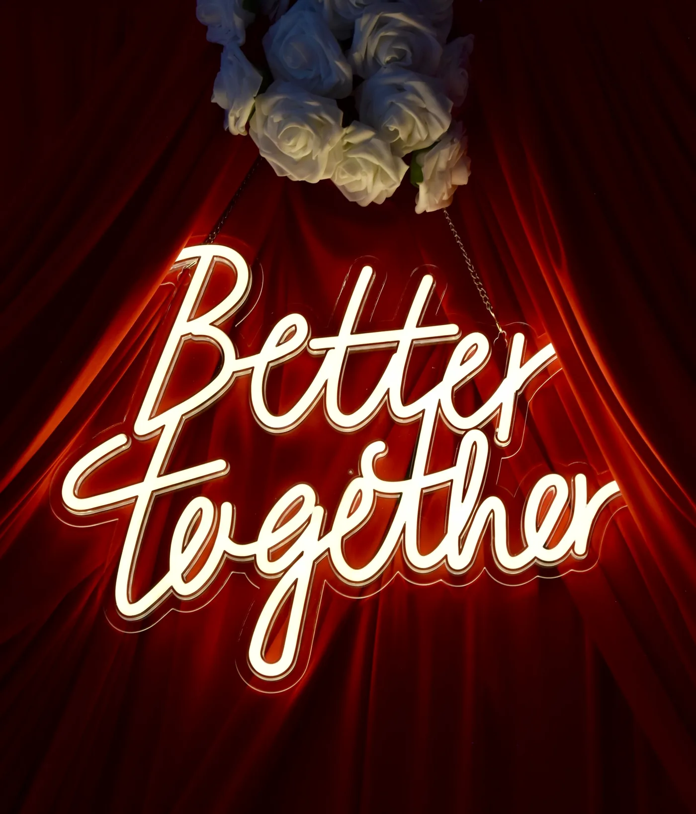 Neon-Schild „Better together“ vor rotem Vorhang mit weißen Rosen